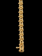 A close-up of a gold tennis bracelet featuring round-cut clear stones in each link, shown vertically against a solid black background.